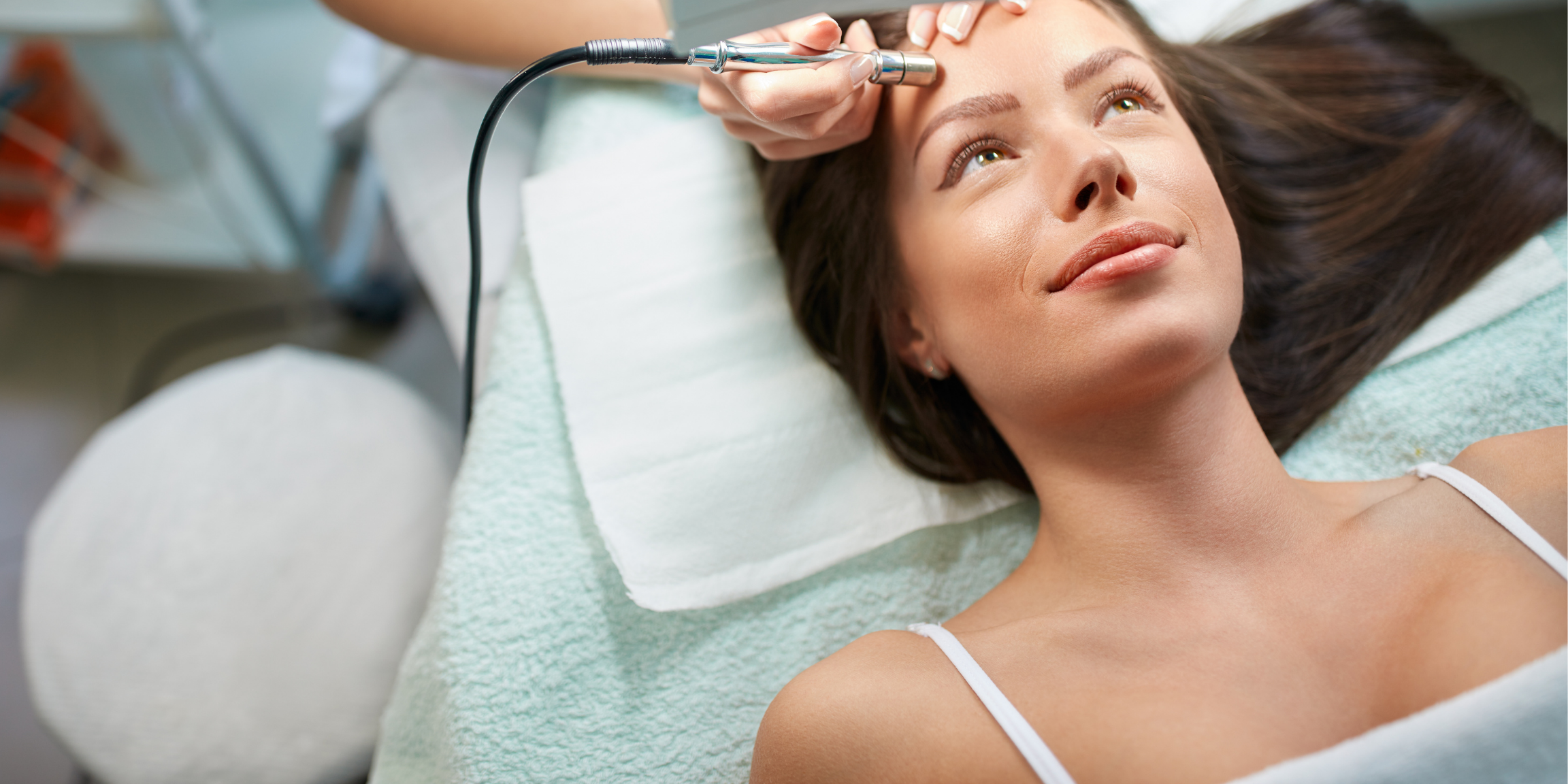 woman smiling, lying down, and receiving a microdermabrasion treatment